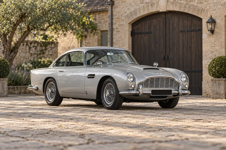 Aston Martin DB5 de collection argentée, carrosserie et jantes à rayons d’origine, dans une cour en pierre